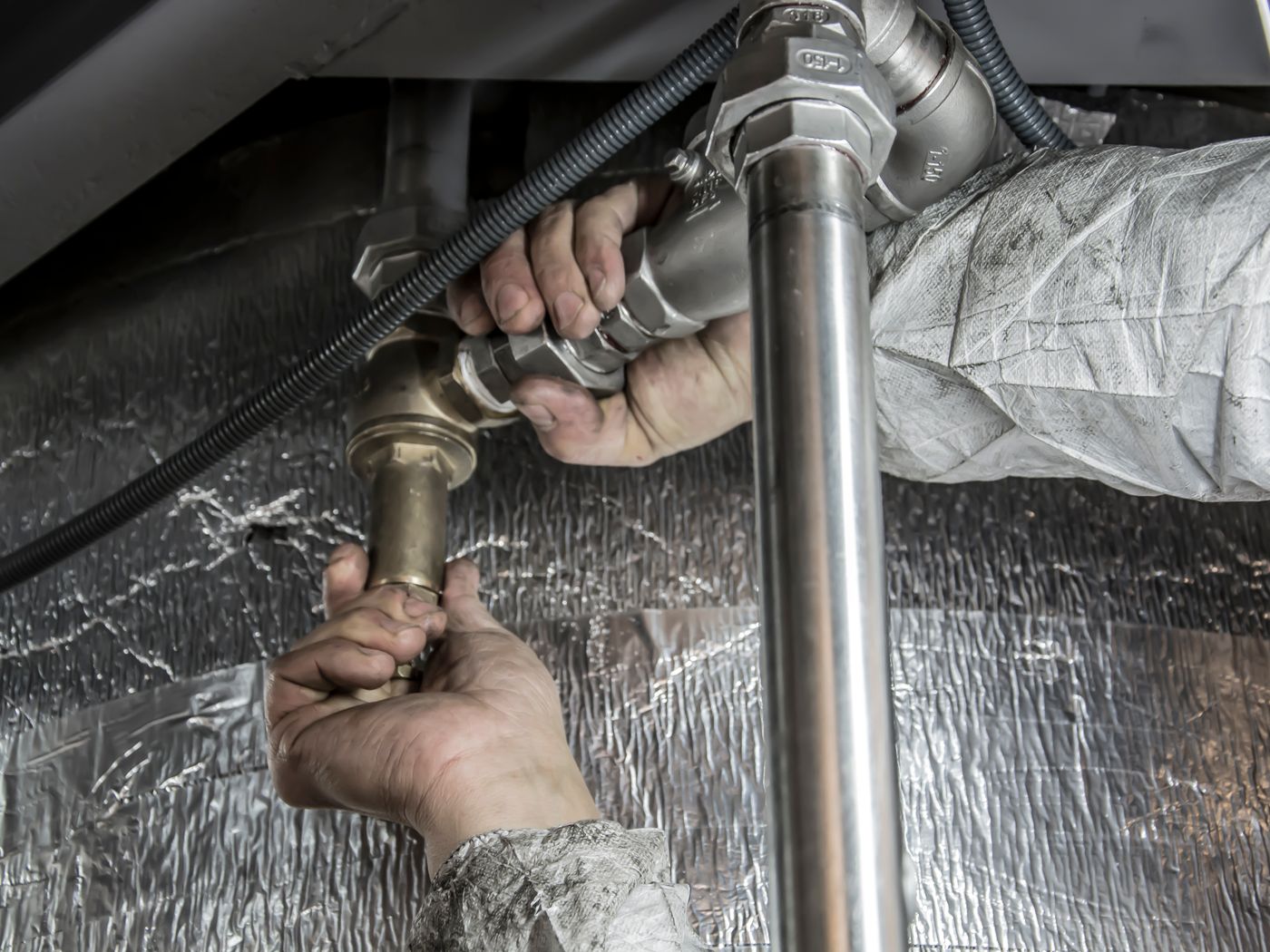Plumber tightening a compression fitting on a supply line beneath insulated subfloor