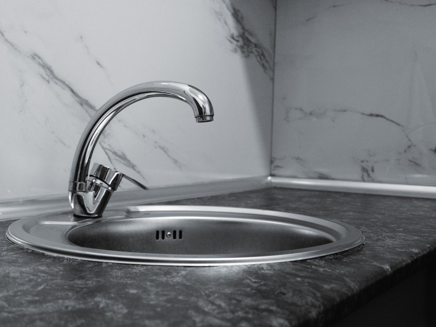 Newly installed stainless kitchen sink and chrome mixer tap on a stone counter